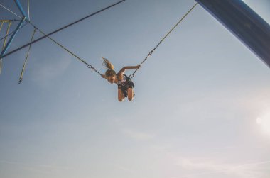 Küçük çocuk bungee jumping 'te eğleniyor. Mavi gökyüzüne doğru yükseliyor.
