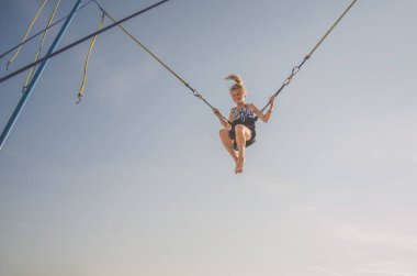 Küçük çocuk bungee jumping 'te eğleniyor. Mavi gökyüzüne doğru yükseliyor.