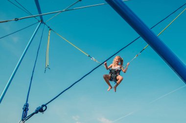 Sevimli genç kız, mavi gökyüzünde sallanırken bungee jumping cazibesinden hoşlanıyor.