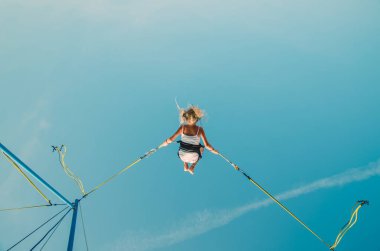 Sevimli genç kız, mavi gökyüzünde sallanırken bungee jumping cazibesinden hoşlanıyor.