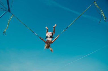 Sevimli genç kız, mavi gökyüzünde sallanırken bungee jumping cazibesinden hoşlanıyor.
