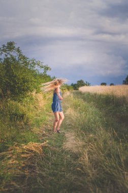 Küçük bir kız, uzun sarı saçlı, korkunç bir öğleden sonra tarlaların arasında dans ediyor.