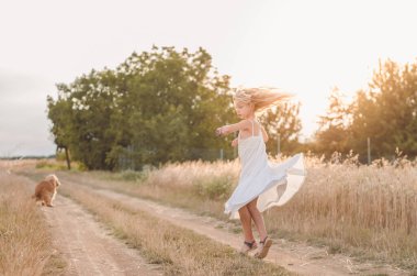 Uzun sarı saçlı kız yaz kırsalında altın saatinde dans ediyor.