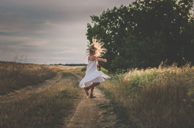 Uzun sarı saçlı kız yaz zamanı dans ediyor kırsal kesimde dramatik bir etki yaratıyor.