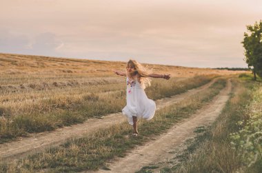 Uzun sarı saçlı çocuk yaz otlaklarında özgürce uçuyor ve dans ediyor.