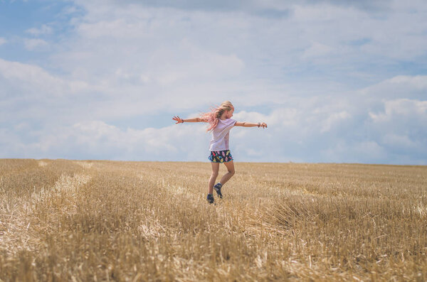 girl with long blond hair spinning around in empty rural field in golden hour time