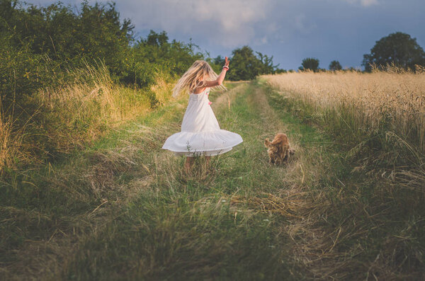 Girl with long blond hair spinning around in magic afternoon escorted by brown domestic dog
