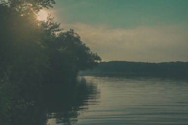 Ağaçların siluetleri ve gölün su yüzeyindeki yansımaları yaz günbatımında