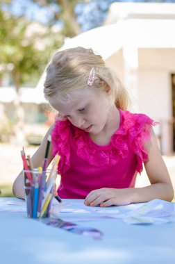 Masada oturan ve kalemle boyayan tatlı bir kız.