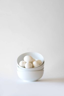 Stack of white bowls with white eggs on white background