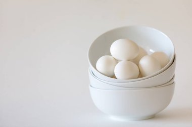 Stack of white bowls with white eggs on white background