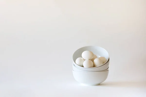 Stack of white bowls with white eggs on white background