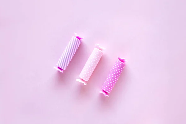 Three candy in polka dot wrapper on pink background. Lip balm sticks.