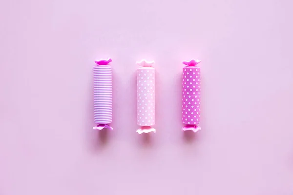 Three candy in polka dot wrapper on pink background. Lip balm sticks.