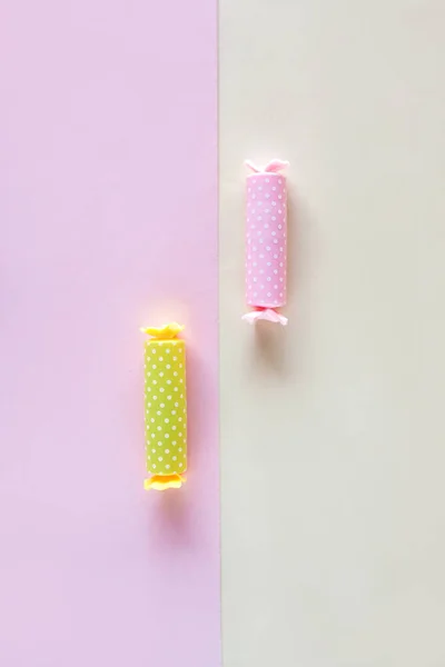 Three candy in polka dot wrapper on pink background. Lip balm sticks.