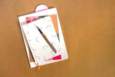 Mürekkep kalemi ve fotokopi alanlarıyla altın kahverengi arka plan üzerine üç defter. Günlük yazma ve not alma kavramı.