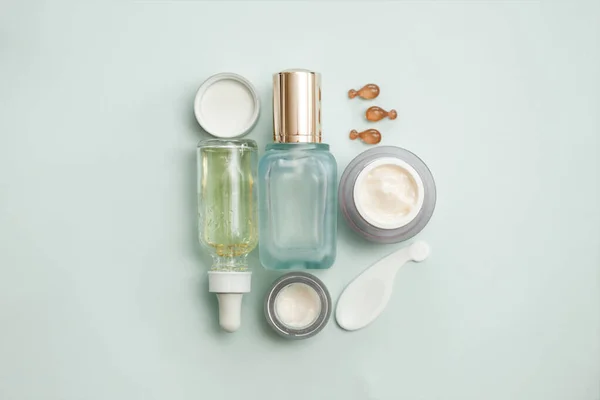 Face serum bottle with face creams, face oil capsules on light teal background. cosmetics flat lay.