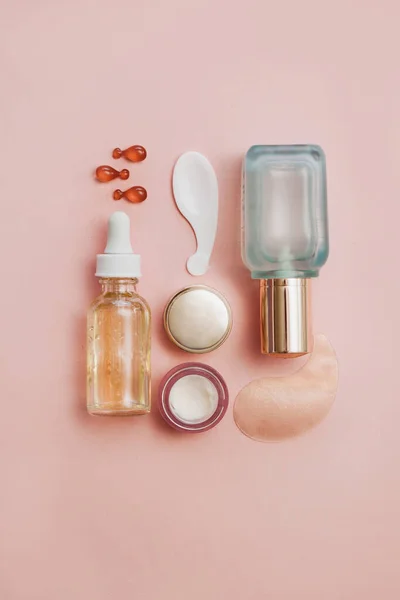 Face serum bottle with face creams, face oil capsules on light pink background. cosmetics flat lay.