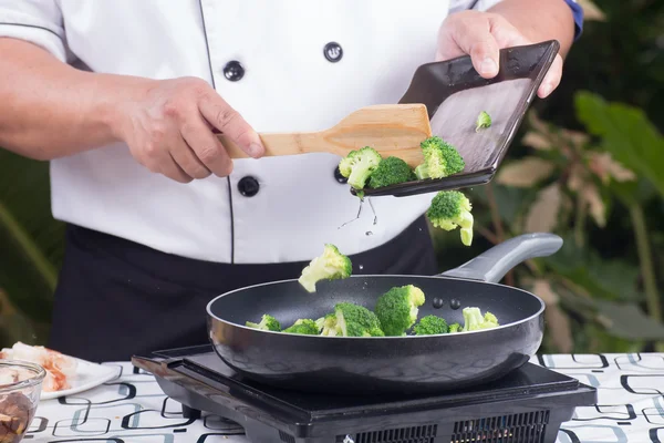 Шеф-повар кладет брокколи на сковородку — стоковое фото