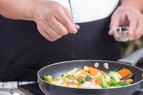 Chef poniendo Sal a la sartén para cocinar verduras — Foto de Stock