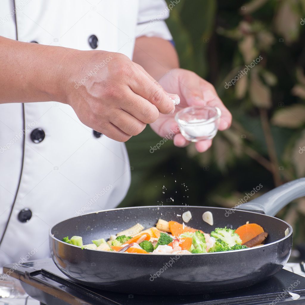 Chef putting Salt to the pan for cooking vegetable
