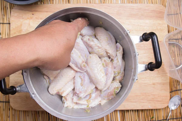 Chef-kok mengen kruiden aan kippenvleugeltjes in pot — Stockfoto