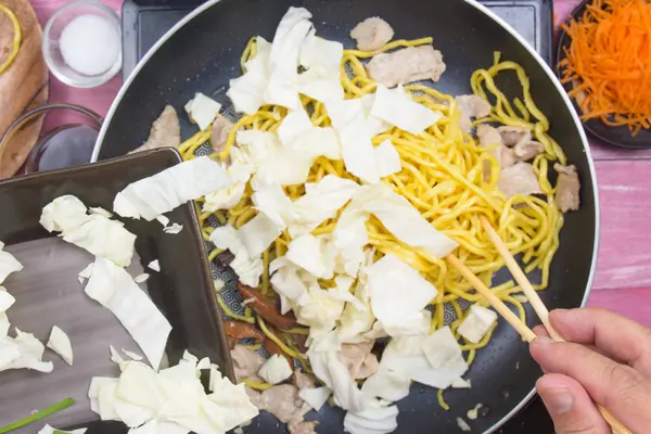 Şef Yakisoba noodle yemek pişirmek için lahana katmak