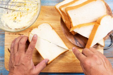 Şef elinde bıçak, tahtadan ekmek kesiyor, tava konseptiyle parmesan peynirli tost pişiriyor.