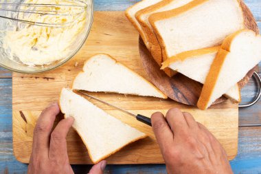 Şef elinde bıçak, tahtadan ekmek kesiyor, tava konseptiyle parmesan peynirli tost pişiriyor.
