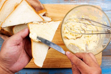 Şef tereyağlı peyniri kaygan ekmeğe sürüp parmesan peynirli tost pişiriyor.