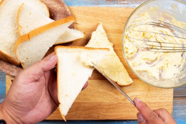 Şef tereyağlı peyniri kaygan ekmeğe sürüp parmesan peynirli tost pişiriyor.