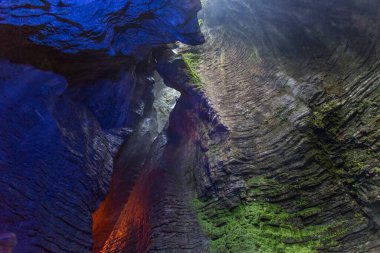 Cascate del Varone ya da Varone Falls, Garda Gölü, İtalya. Bir şelalenin ıslak kayalıklarında yeşil yosun bulunan mavi ve kırmızı ışıklarla aydınlatılmış bir mağara kayaları.