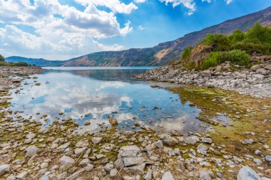 Ayna su yüzeyi. Nemrut yanardağının Ili Gölü panoramik manzarası, Bitlis ilinin, Doğu Türkiye. Göldeki bulutlu gökyüzünün yansıması. Taş taban berrak sularda