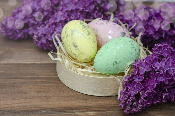 Paskalya yumurtaları ve eski ahşap arka plan üzerinde taze leylak çiçekler
