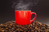 Červený šálek horké kávy s párou na pražených kávových zrnech a tmavým pozadím. Šálek horké kávy s kouřem na kávovém pozadí.