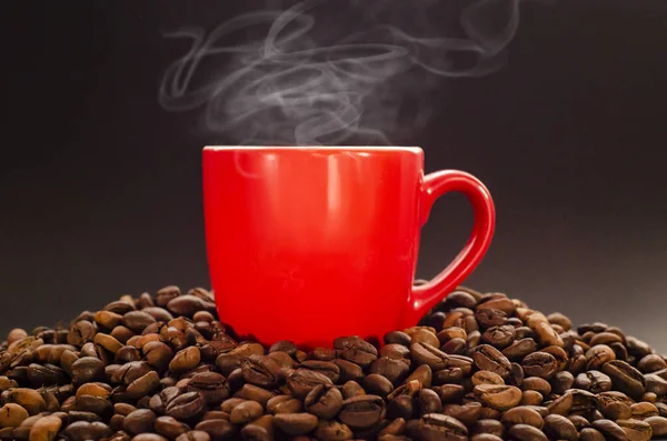 Kavrulmuş kahve çekirdekleri ve koyu arkaplanda kaynayan bir fincan sıcak kahve. Kahve fonda sigara dumanı olan bir fincan sıcak kahve..