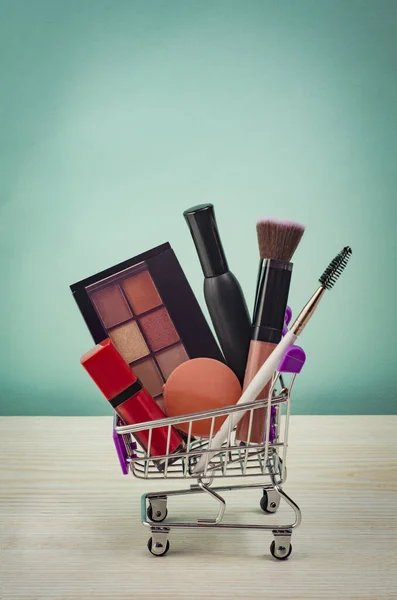 Mavi arka planda makyaj ve kozmetik ürünlerle dolu bir alışveriş arabası. Kara Cuma konsepti. İndirim ve indirim. Kadınlar için mallar. Makyaj ürünleri olan bir sepetin kapanışı. 