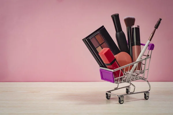 Makyaj arabaları ve pembe arka planda kozmetik ürünler. Kara Cuma konsepti. İndirim ve indirim. Kadınlar için mallar. Makyaj ürünleri olan bir sepetin kapanışı. 