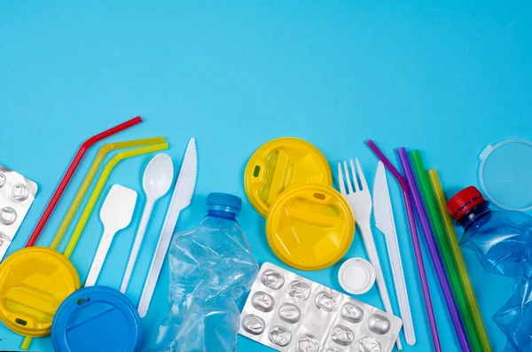 White single-use plastic and other plastic items on a blue background. The concept of choice without plastic or environmental problems.