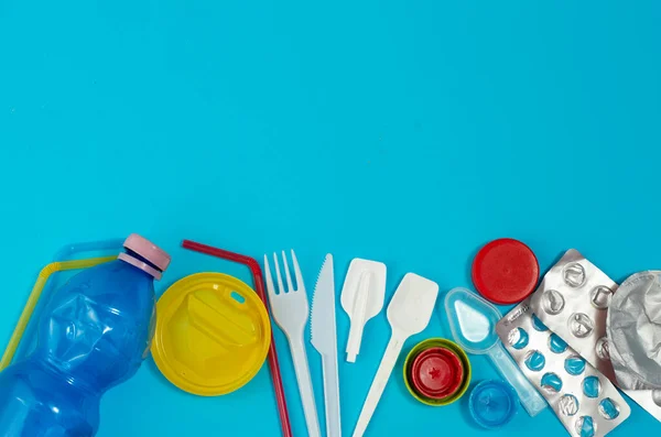 White single-use plastic and other plastic items on a blue background. The concept of choice without plastic or environmental problems.
