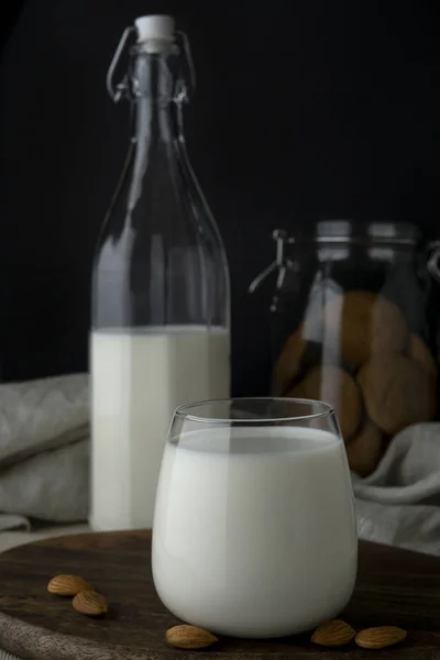 Un vaso de leche transparente, una botella de leche, almendras y galletas —  Fotos de Stock