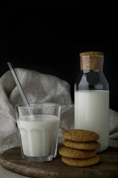 Un vaso de leche, una botella de leche y galletas de avena en la tabla de cortar —  Fotos de Stock
