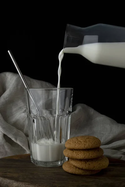 Melk wordt gegoten in een glas uit een transparante fles, haverkoekjes — Stockfoto