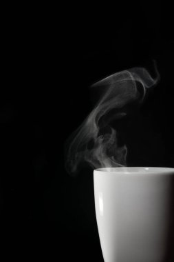 Siyah arkaplanda buharı olan beyaz kupa