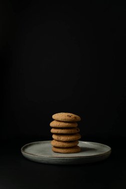 Stack of oatmeal cookies on a clay plate in the dark