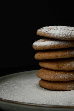 Stack of oatmeal cookies with powdered sugar on a clay plate on dark background