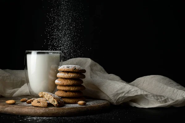 Galletas de avena con chocolate, almendras, leche en vaso con paredes dobles, espolvorear azúcar en polvo sobre tela blanca —  Fotos de Stock