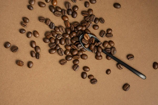 Alguns grãos de café com uma colher de metal preto em uma superfície marrom — Fotografia de Stock