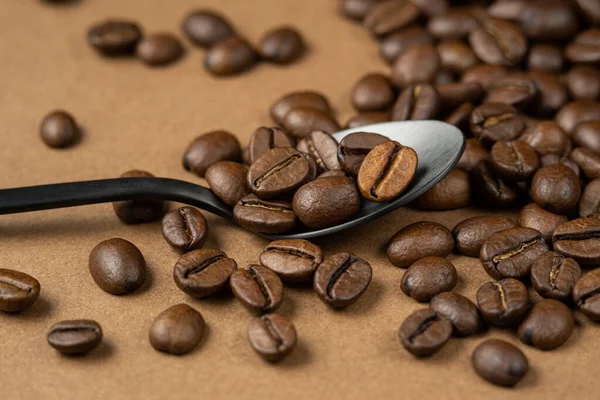 Grains de café en métal noir cuillère sur une surface brune — Photo