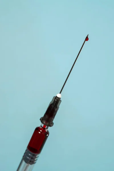 Syringe with red liquid and red drop at the end of the needle